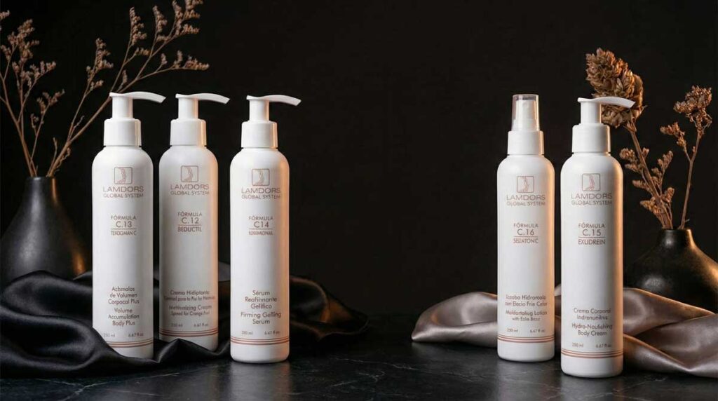 Cinco botellas blancas de productos Lamdors para el cuidado de la piel están dispuestas sobre una superficie oscura con cortinas de tela neutra y plantas secas de fondo.